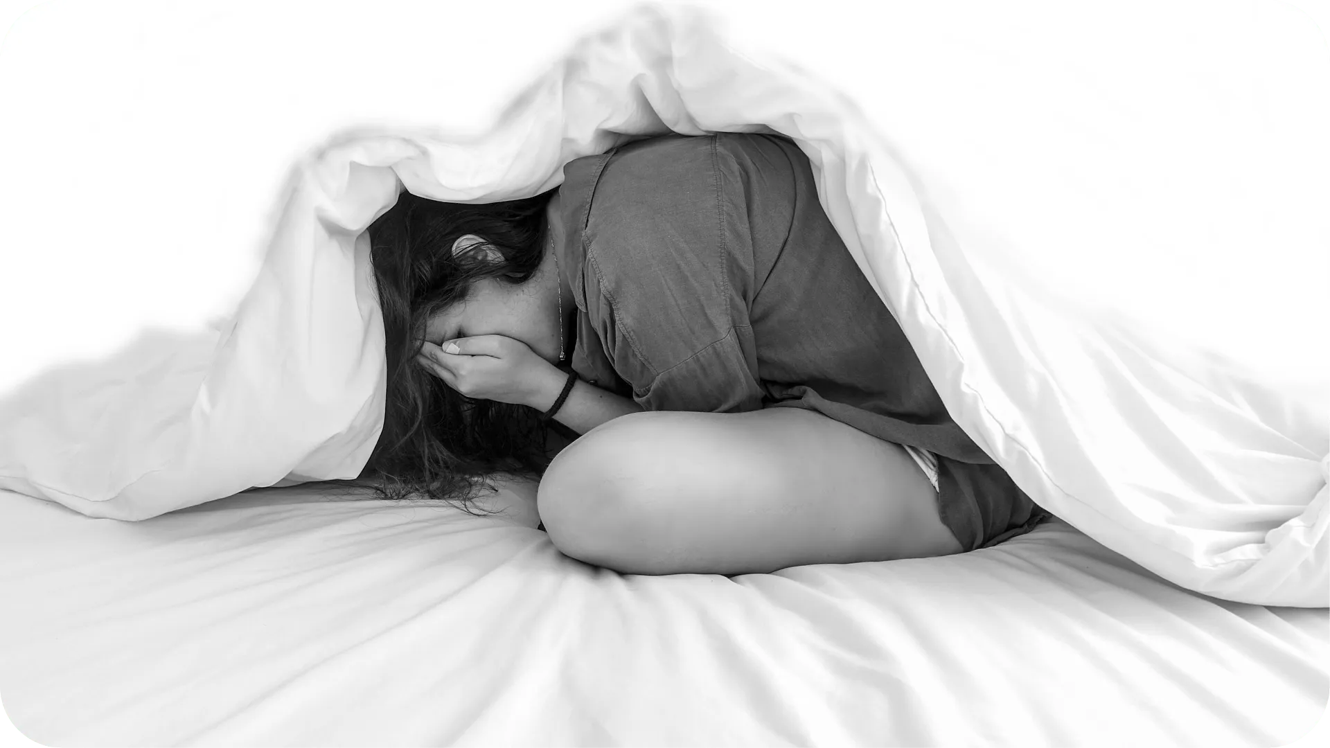 Black and white photo of a person looking upset and hiding in their bed due to anxiety.