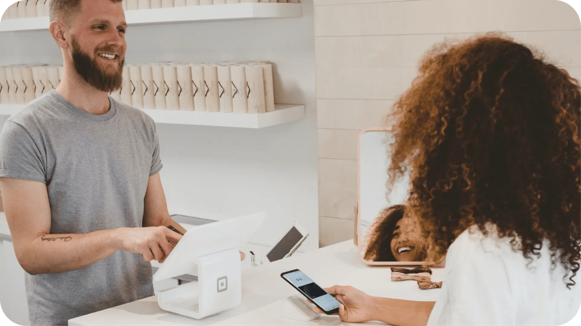 A woman buying something from a man who works behind the till in a shop.