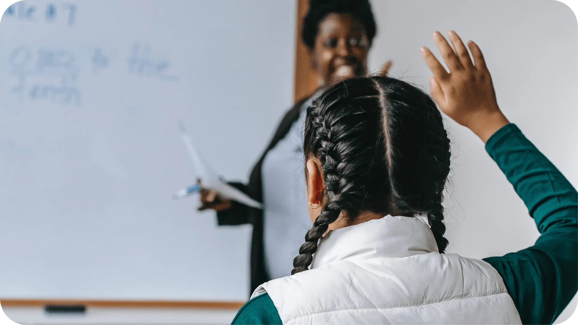A young girl raises her hand at school to answer a question.